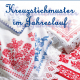 Cover des Buches 'Kreuzstichmuster im Jahreslauf' mit roten und blauen Mustern bestickten Stoffen