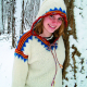 Weibliche Person in einer Schneelandschaft, die einen Norwegerpullover mit Kapuze in weiß/balu/rot anhat.