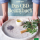 Cover des Buches 'Das CBD Beautybuch' mit einem runden Tablett, auf dem gefüllte Tasse, Blätter und Hanfsamen liegen