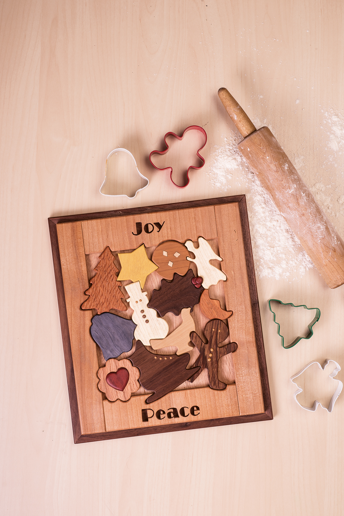 Ein viereckiges Holzpuzzle mit winterlichen Motiven wie Schneemann, Engel, Glocke oder Tannenbaum