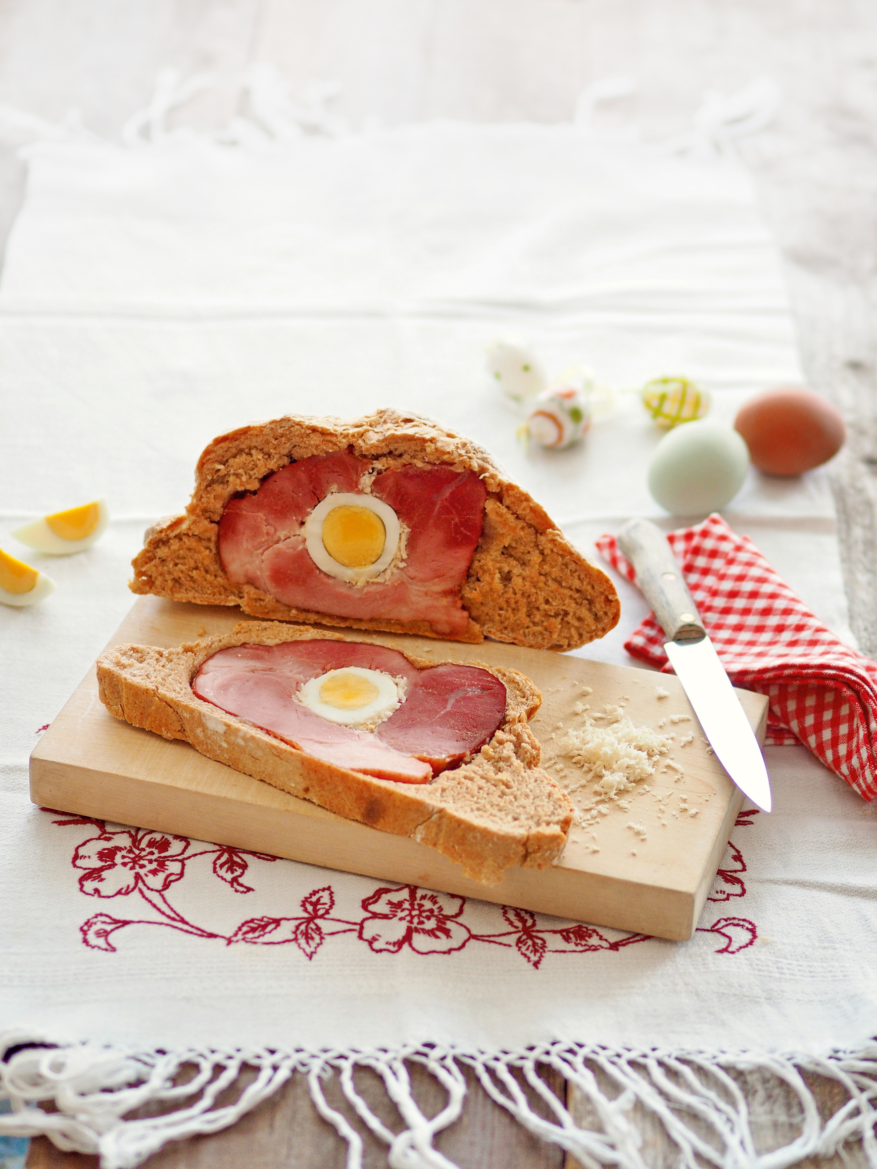 Eine Scheibe des Osterschinken im Brotteigmantel liegt auf einem Holzbrett, daneben der Rest des Brotes