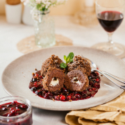 Drei Schokoladen-Topfenknödel angerichtet auf einem weißen Teller mit Beerenragout auf einem gedeckten Tisch