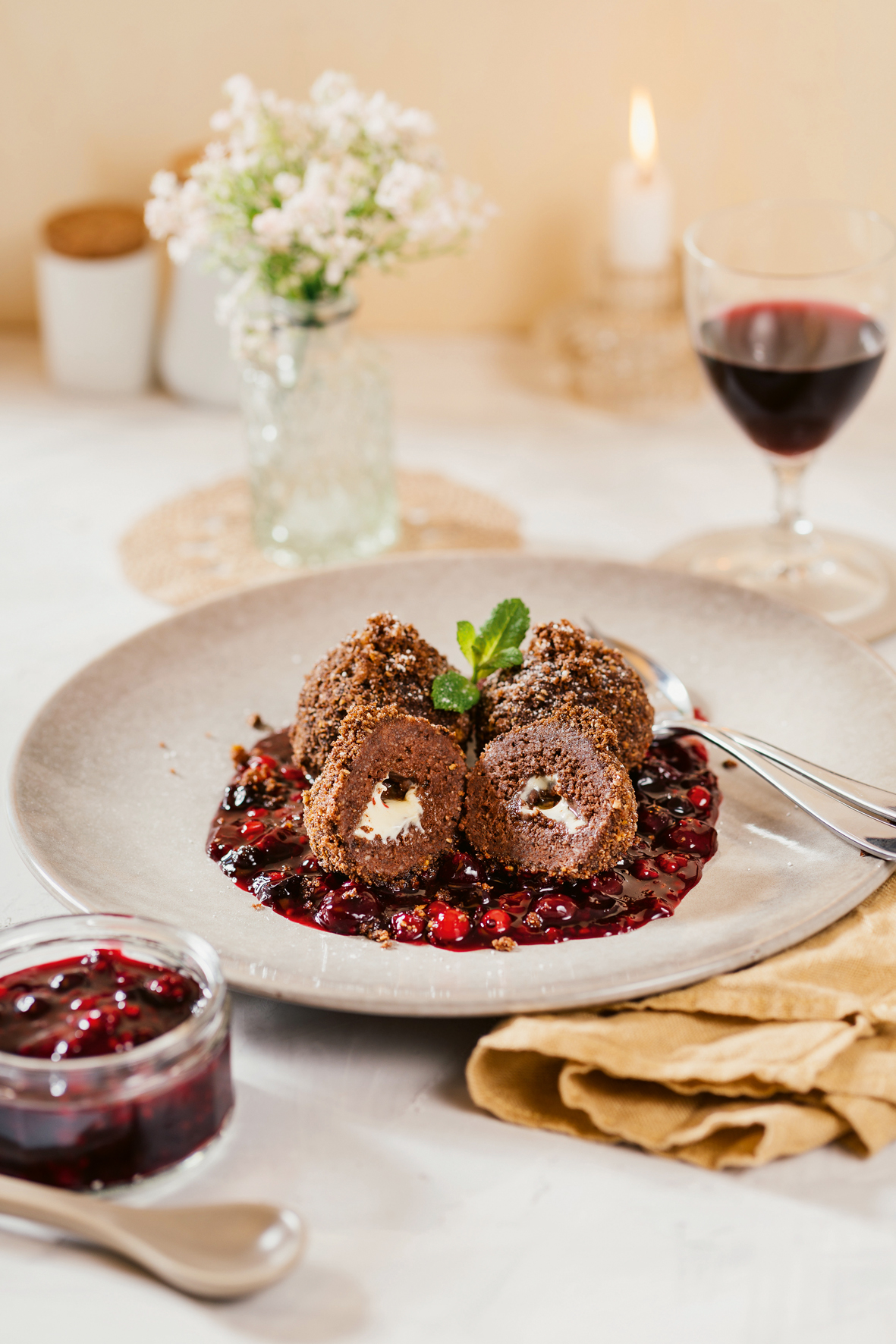 Drei Schokoladen-Topfenknödel angerichtet auf einem weißen Teller mit Beerenragout auf einem gedeckten Tisch