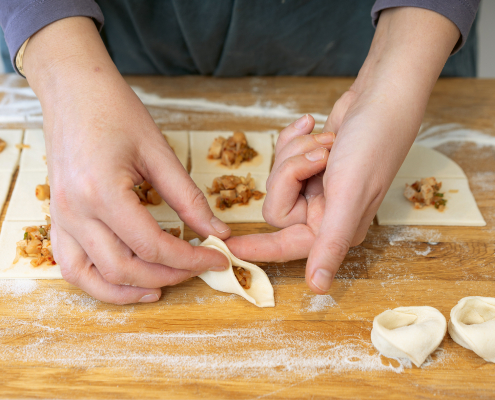 zwei Hände, die das gefüllte Tortelliniteigquadrat zusammendücken