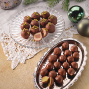 ein silbernes Tablett sowie ein Glasteller, auf denen viele Nougat-Marzipan Kugeln liegen. Daneben weihnachtliche Deko