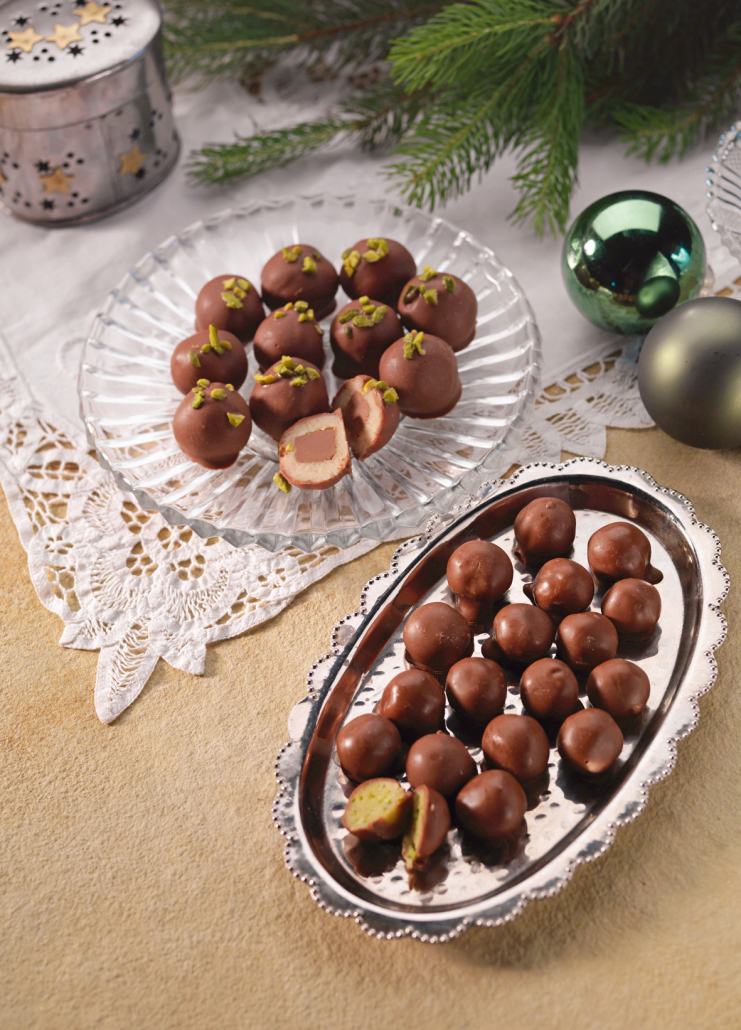 ein silbernes Tablett sowie ein Glasteller, auf denen viele Nougat-Marzipan Kugeln liegen. Daneben weihnachtliche Deko