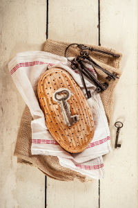 Ein Laib Brot mit mit einem Schlüssel an der Brotoberseite liegt auf einer Serviette, daneben ein alter Schlüsselbund.