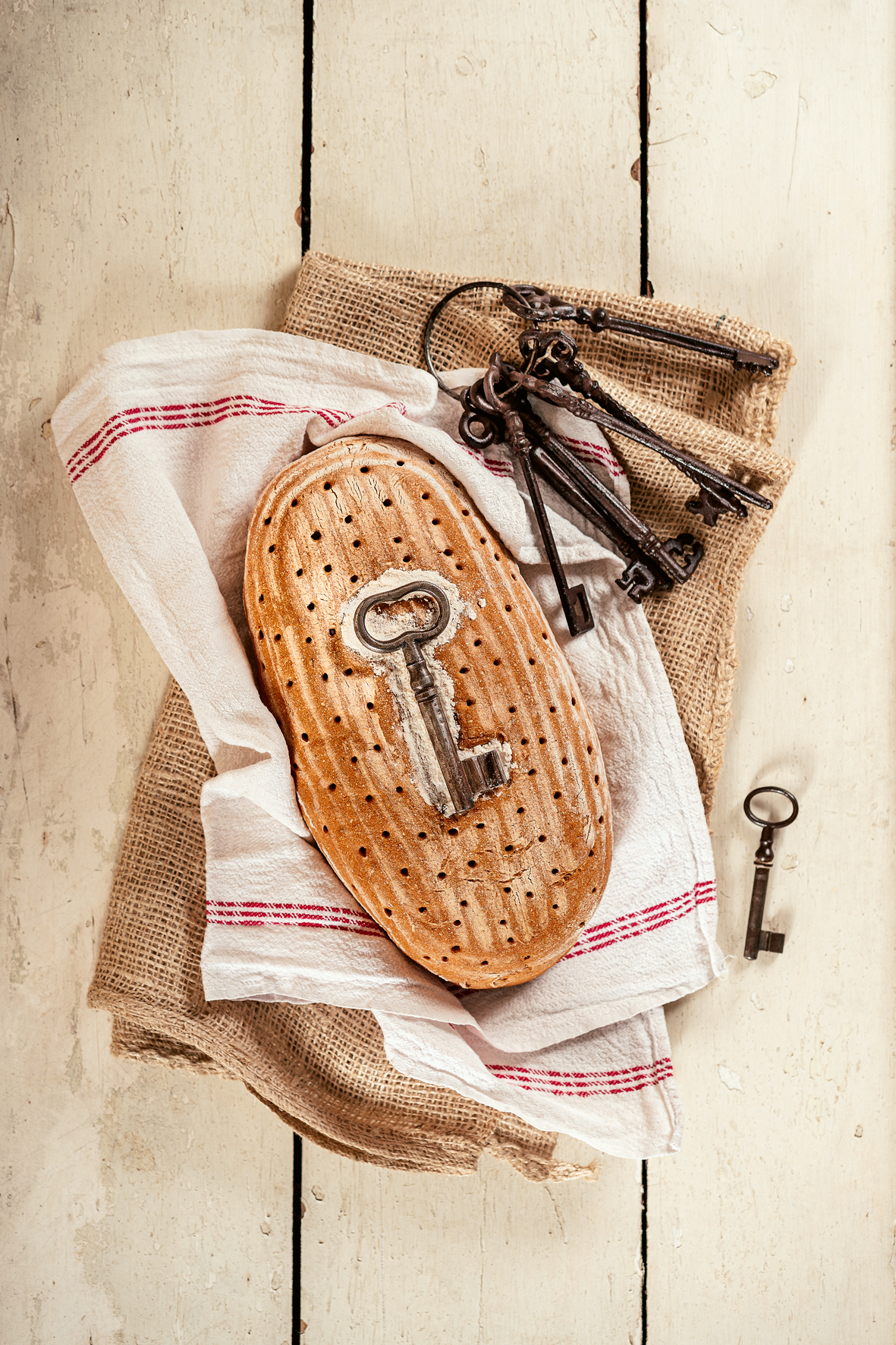 Ein Laib Brot mit mit einem Schlüssel an der Brotoberseite liegt auf einer Serviette, daneben ein alter Schlüsselbund.