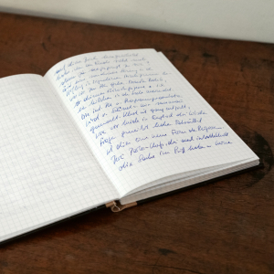 aufgeschlagenes Notizheft, bei dem die rechte Seite handschriftlich beschrieben wurde