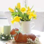 Ein Kuchen in Form eines Osterlamms auf einem Holzbrett, das auf einem frühlingshaft dekorierten Tisch steht