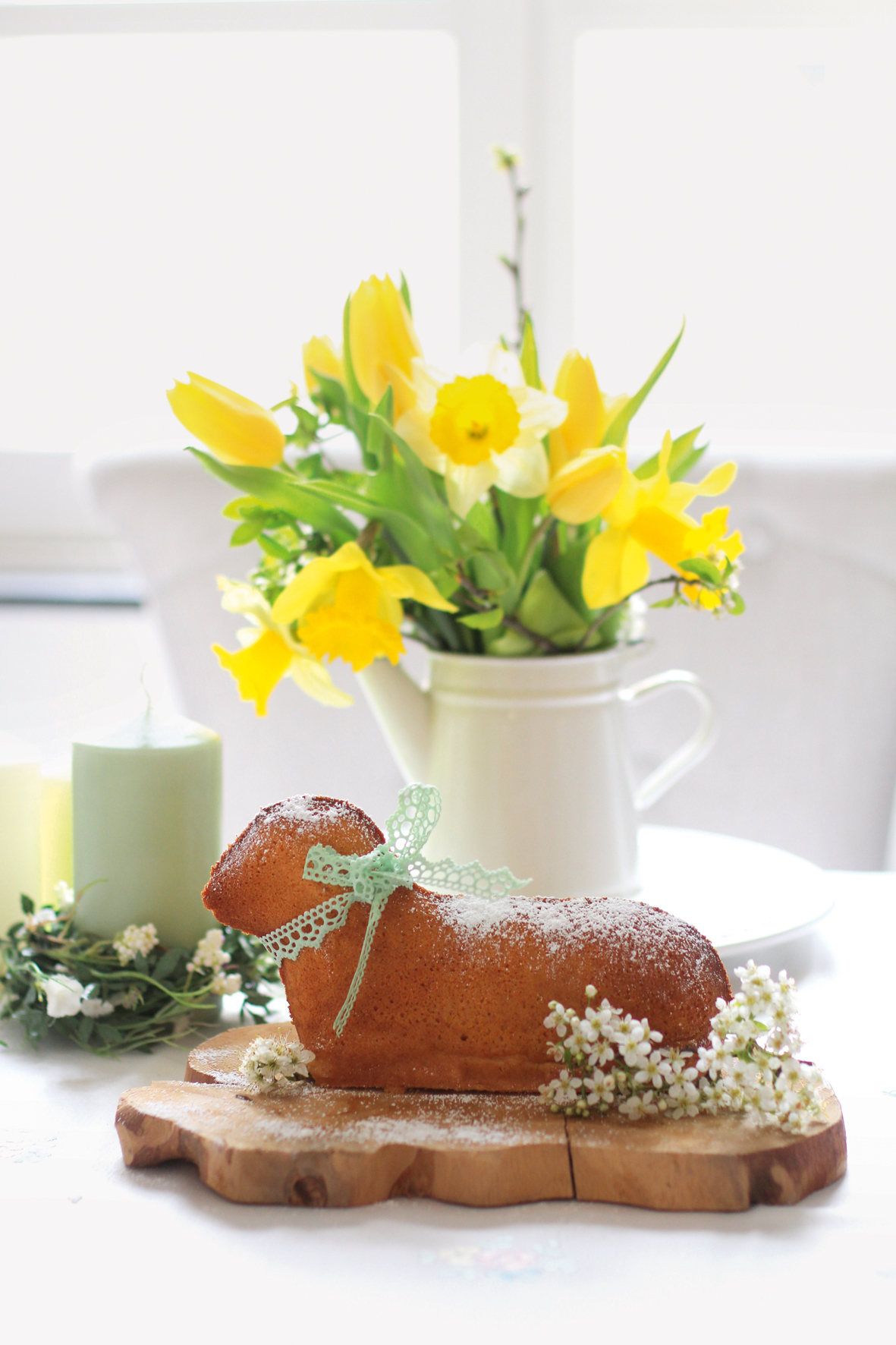 Ein Kuchen in Form eines Osterlamms auf einem Holzbrett, das auf einem frühlingshaft dekorierten Tisch steht