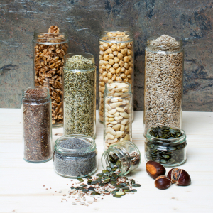 Verschieden große Vorratsglässer gefüllt mit Walnüssen, Leinsamen, Mohn, Haselnüssen, Mandeln, Sonnenblumenkernen, Kürbiskernen und Hanfsamen.
