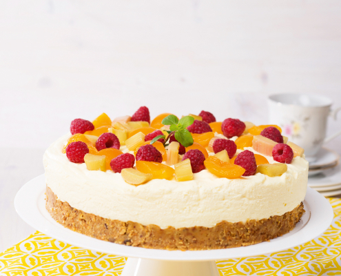 cremig-fruchtige Torte auf weißem Tortenteller platziert, garniert mit vielen Früchten