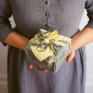 Eine Person hält ein Geschenk welches in einem selbst gefärbten Tuch eingewickelt ist.