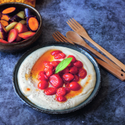 Ein dunkler Teller auf dem die Aioli angerichtet ist, darauf sind Tomaten platziert. Neben dem Teller liegt ein Holzbesteck