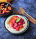 Ein dunkler Teller auf dem die Aioli angerichtet ist, darauf sind Tomaten platziert. Neben dem Teller liegt ein Holzbesteck