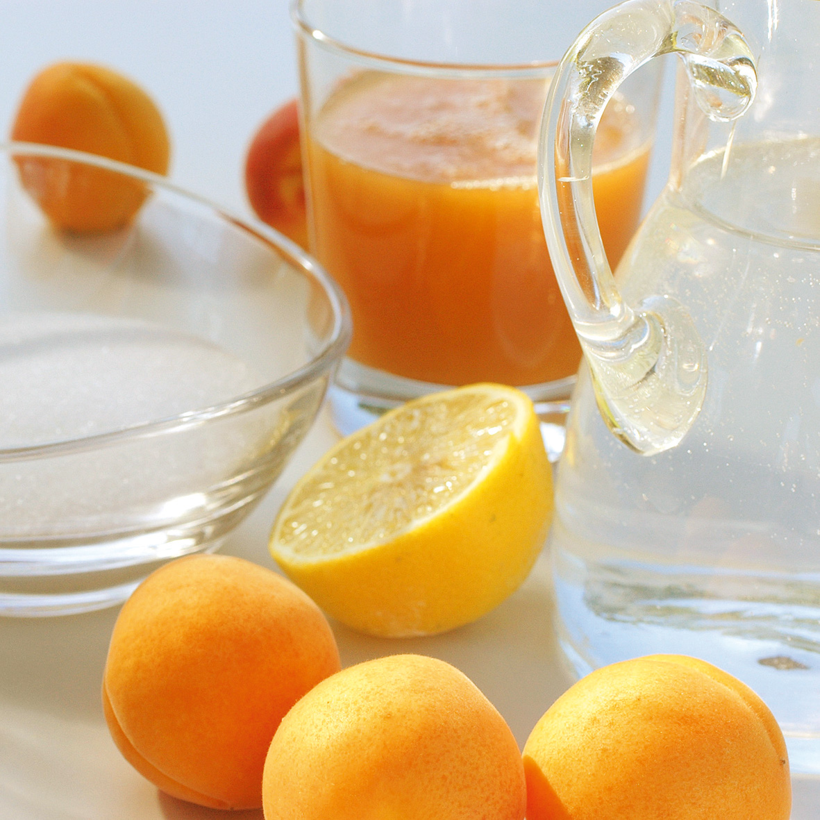 Ein Glas mit Fruchtsaft, davor liegen Orangen und Marille