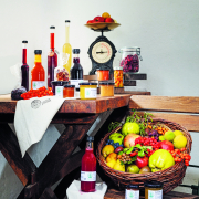 Ein Holztisch, auf dem viele Obstsaftflaschen und Marmeladegläser stehen. Daneben ein Holzsessel, auf dem ein Korb mit frischem Obst und Gemüse steht