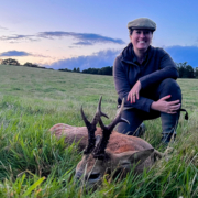Eine Frau, die auf einer großen grünen Landschaft neben einem toten Rehbock hockt.