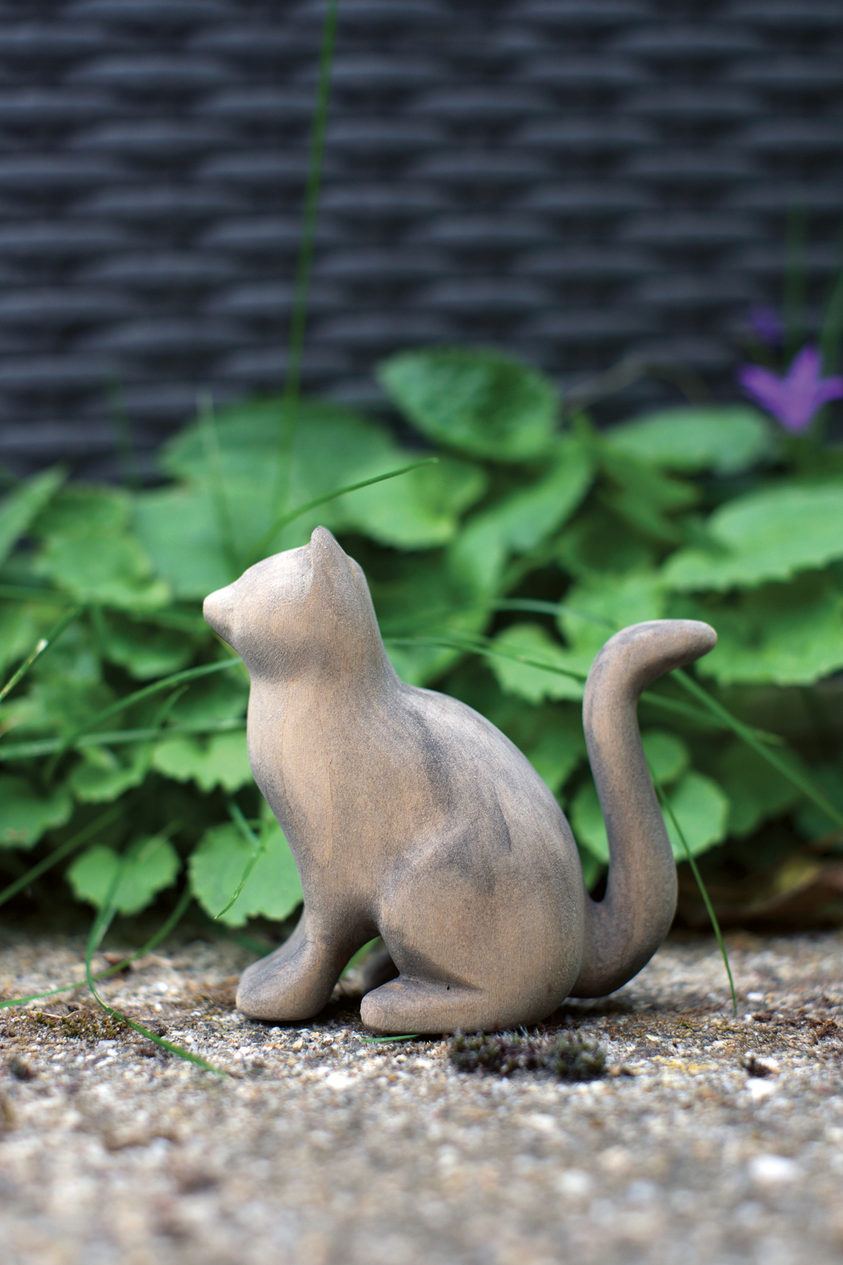 Eine sitzende, aus Holz geschnitzte Katze vor einer grünen Pflanze. Eine sitzende, aus Holz geschnitzte Katze vor einer grünen Pflanze.