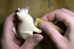 Die aus Holz geschnitzte Katze wird mit Schleifpapier bearbeitet Die aus Holz geschnitzte Katze wird mit Schleifpapier bearbeitet