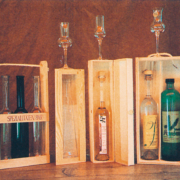 Mehrere Holzbehälten mit Flaschen gefüllt mich verschiedenen Schnäpsen. Drei Schnapsgläser stehen als Dekoration daneben