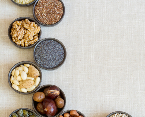 Insgesamt neun schwarze kleine Schälchen, die verschiedene Samen und Nüsse enthalten. Es sind Walnüsse, Mandeln, Haselnüsse, Leinsamen, Hanfsamen, Maroni, Mohn, Sonnenblumen- und Kürbikerne.