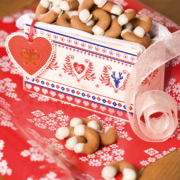 Eine weiß-rot-blaue Pappschachtel gefüllt mit Kaffeekipferl, die auf rotem Geschenkspapier steht.