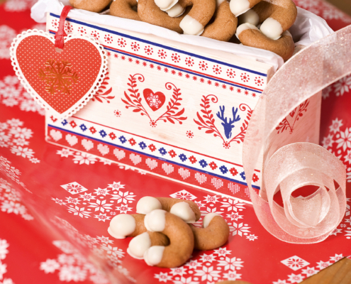 Eine weiß-rot-blaue Pappschachtel gefüllt mit Kaffeekipferl, die auf rotem Geschenkspapier steht.