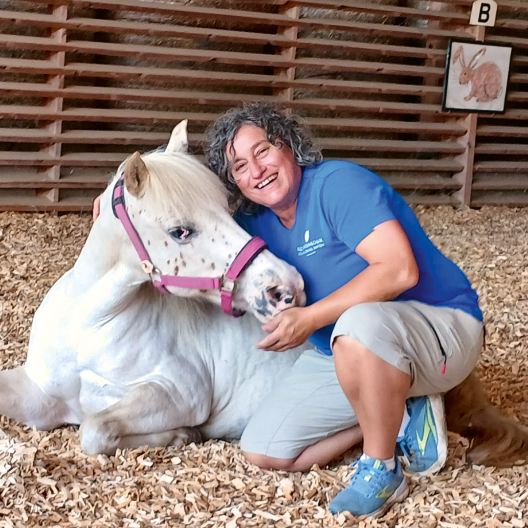 Die Autorin kniet neben einem liegenden weißem Pferd