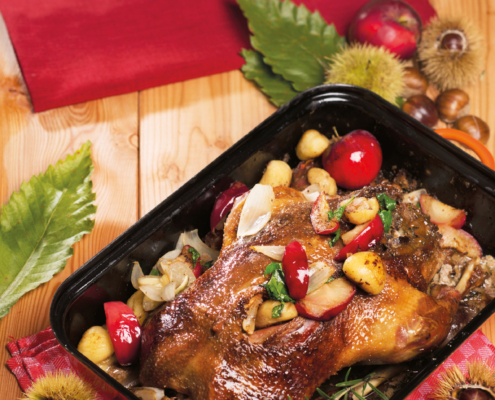 Eine gebratene Gans mit Gemüse liegt in einer rechteckigen Kaserolle.