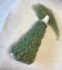 Fantastisches Nadelfilzen37_C_Claudia Marie Lenart -6 Ein grüner Filzkegel, bei dem die weiße Spitze rausschaut. Auf der Spitze liegt ein grünes Stück Wolle.