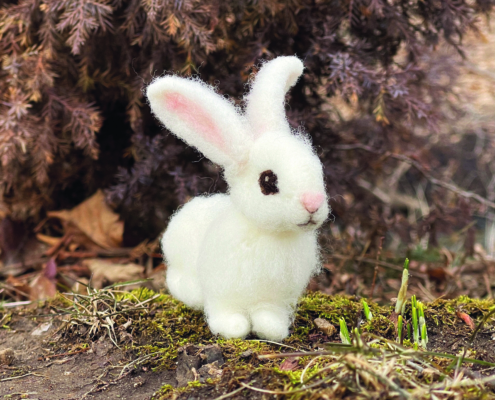 Ein kleines weißes gefilztes Kaninchen, das auf einem Waldboden sitzt.