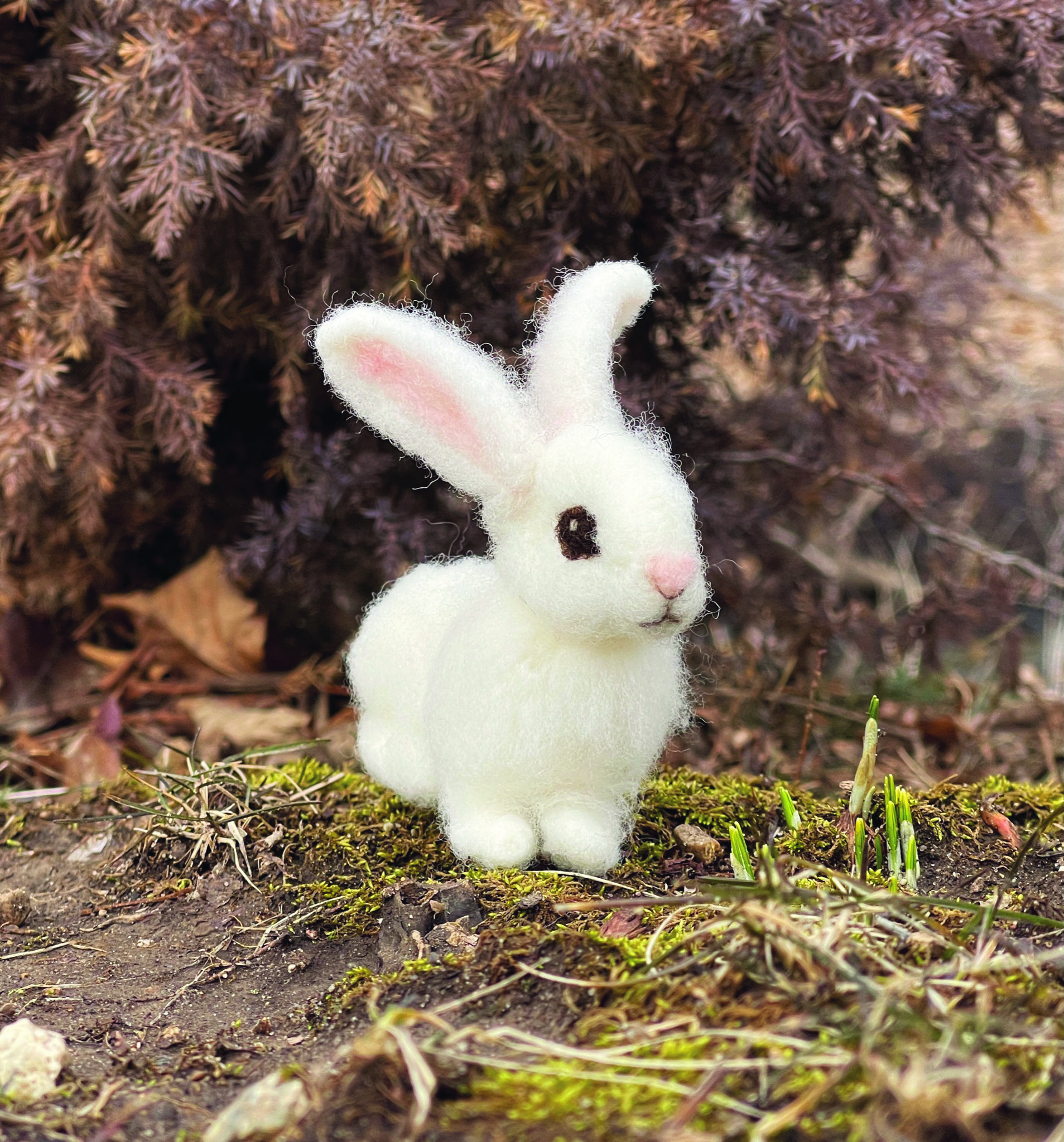 Ein kleines weißes gefilztes Kaninchen, das auf einem Waldboden sitzt.