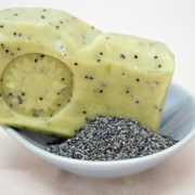 Ein Stück Mohnseife liegt auf einem weißen Teller, daneben ein kleines Häufchen Mohn