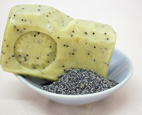 Ein Stück Mohnseife liegt auf einem weißen Teller, daneben ein kleines Häufchen Mohn