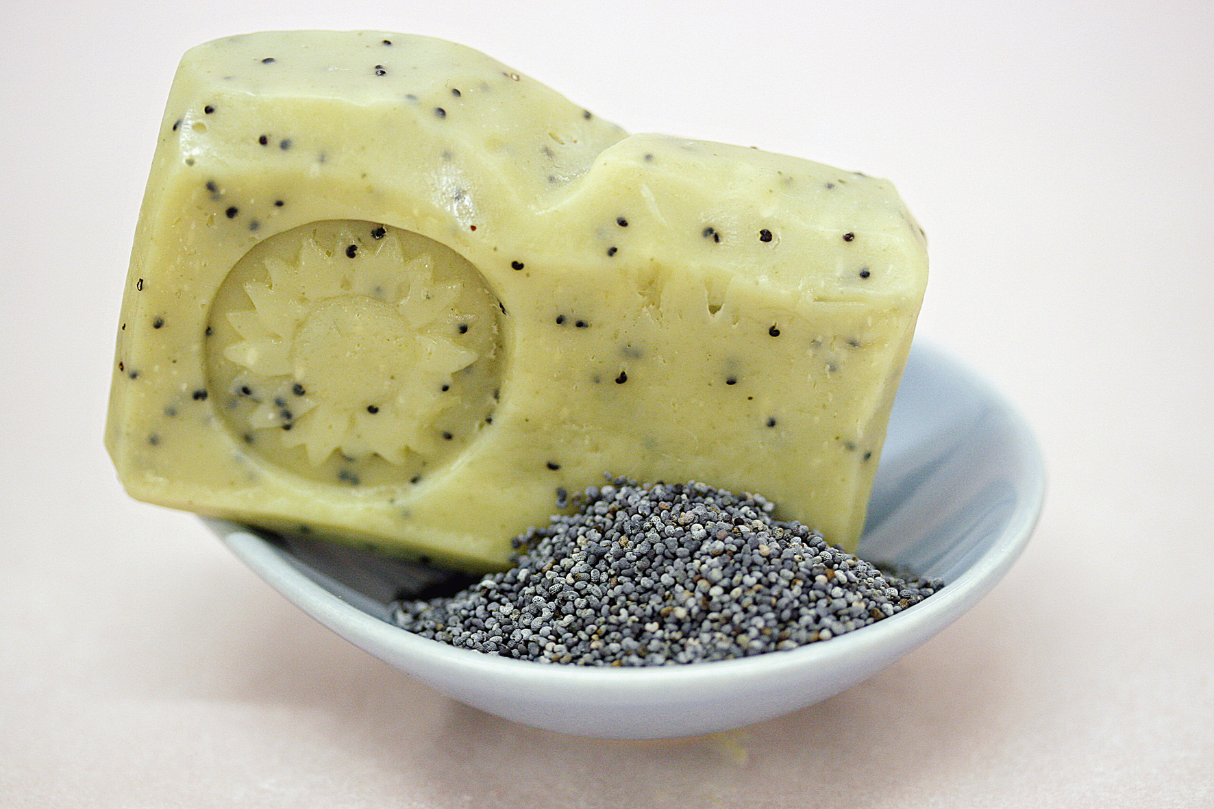 Ein Stück Mohnseife liegt auf einem weißen Teller, daneben ein kleines Häufchen Mohn