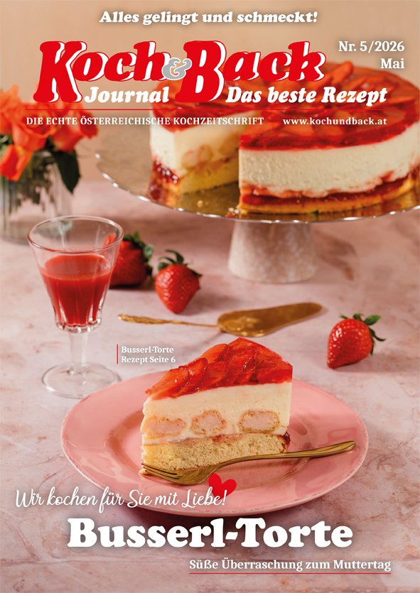Cover des Koch und Back Journals mit einem Tortenstück auf einem Teller, auf einem gedeckten Tisch mit einem befüllten Glas, Erdbeeren und eine angeschnittene Torte und Blumenstrauß im Hintergrund