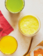 Man sieht drei Gläser von oben, eines mit einem grünen, eines mit einem gelben und eines mit einem orangen Saft befüllt.