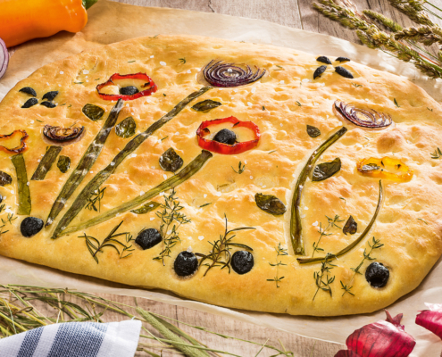 Ein Flammkuchen auf dem mit Kräutern und Gemüse eine Blumenwiese abgebildet ist.