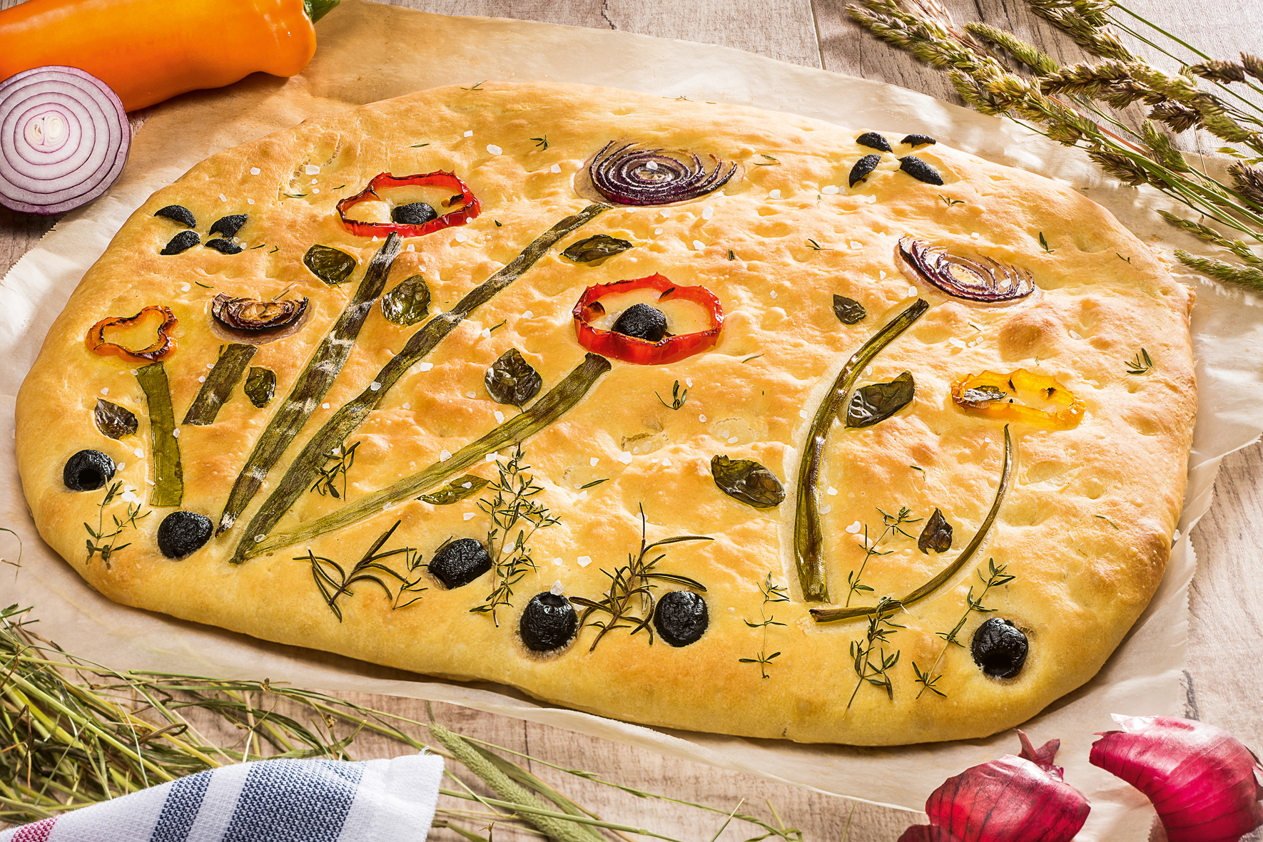 Ein Flammkuchen auf dem mit Kräutern und Gemüse eine Blumenwiese abgebildet ist.