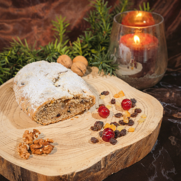 2 Ein angeschnittener Stollen auf einem Holzschneidbrett, darauf auch Walnusskerne, Dörrzwetschken und Feigen. Dahinter Tannenzweige und ein Glas mit einem angezündeten Teelicht
