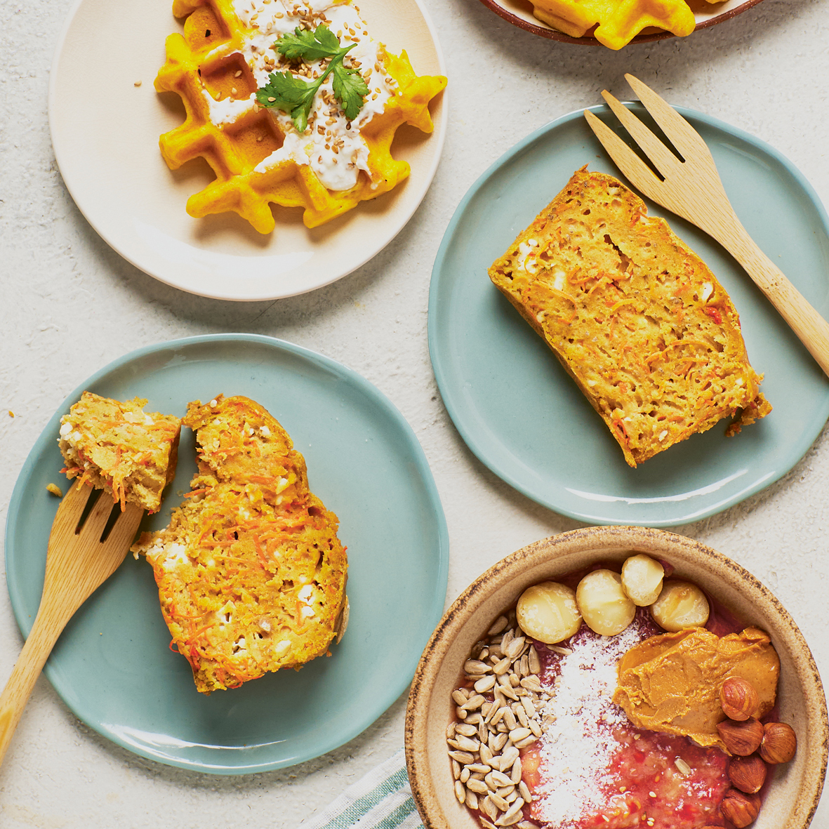 Mehrere Teller mit Waffeln, Kuchen und eine Frühstücks-Bowl auf einem Tisch